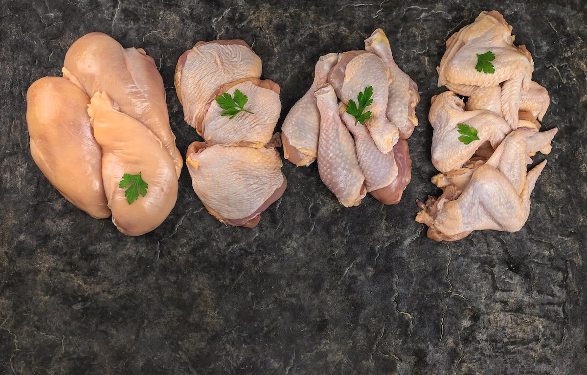 Rôzne časti surového kuracieho mäsa – prsia, stehná a krídla na pracovnej doske