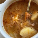 Kapustová polievka s klobásou a zemiakmi v bielej miske, hustá domáca polievka s kúskami mäsa a kapusty