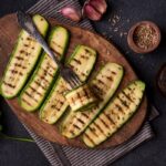 Grilovaná cuketa nakrájaná na plátky s grilovacími pruhmi na drevenej doske