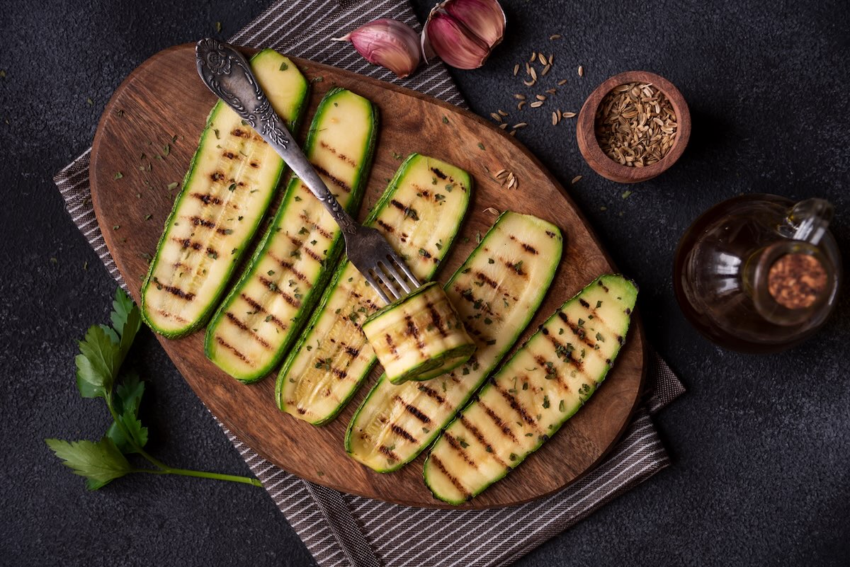 Grilovaná cuketa nakrájaná na plátky s grilovacími pruhmi na drevenej doske