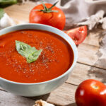 Paradajková polievka s ryžou ozdobená čerstvou bazalkou a čiernym korením v bielej miske s paradajkami a cesnakom