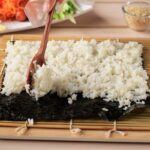 Ako uvariť ryžu na sushi (jednoduchý postup) Ryža na sushi rozložená na nori riasu pri príprave domácich sushi roliek