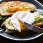 Vajcia Benedikt ako z reštaurácie Vajcia Benedikt s avokádom na toaste s roztečeným žĺtkom