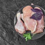 Surové kuracie mäso na tmavom tanieri – vykostené stehná a kuracie prsia s fialovým bazalkou a petržlenovou vňaťou