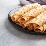 Tenké zrolované palacinky na čiernom tanieri na sivom podklade