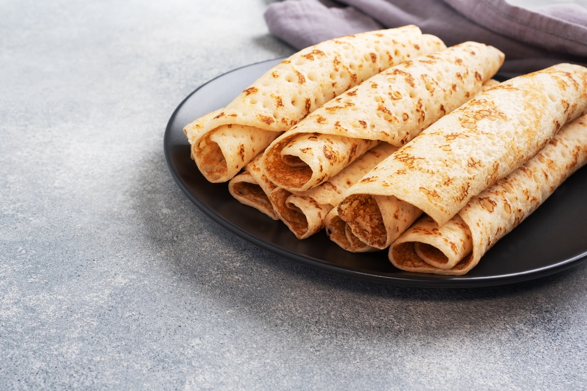 Tenké zrolované palacinky na čiernom tanieri na sivom podklade