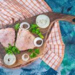 Surové vykostené kuracie stehná na drevenej doske s cibuľovými krúžkami a petržlenovou vňaťou