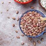 Rôzne druhy suchých strukovín v miskách — pestrá fazuľa, biela fazuľa a šošovica s drevenou lopatkou