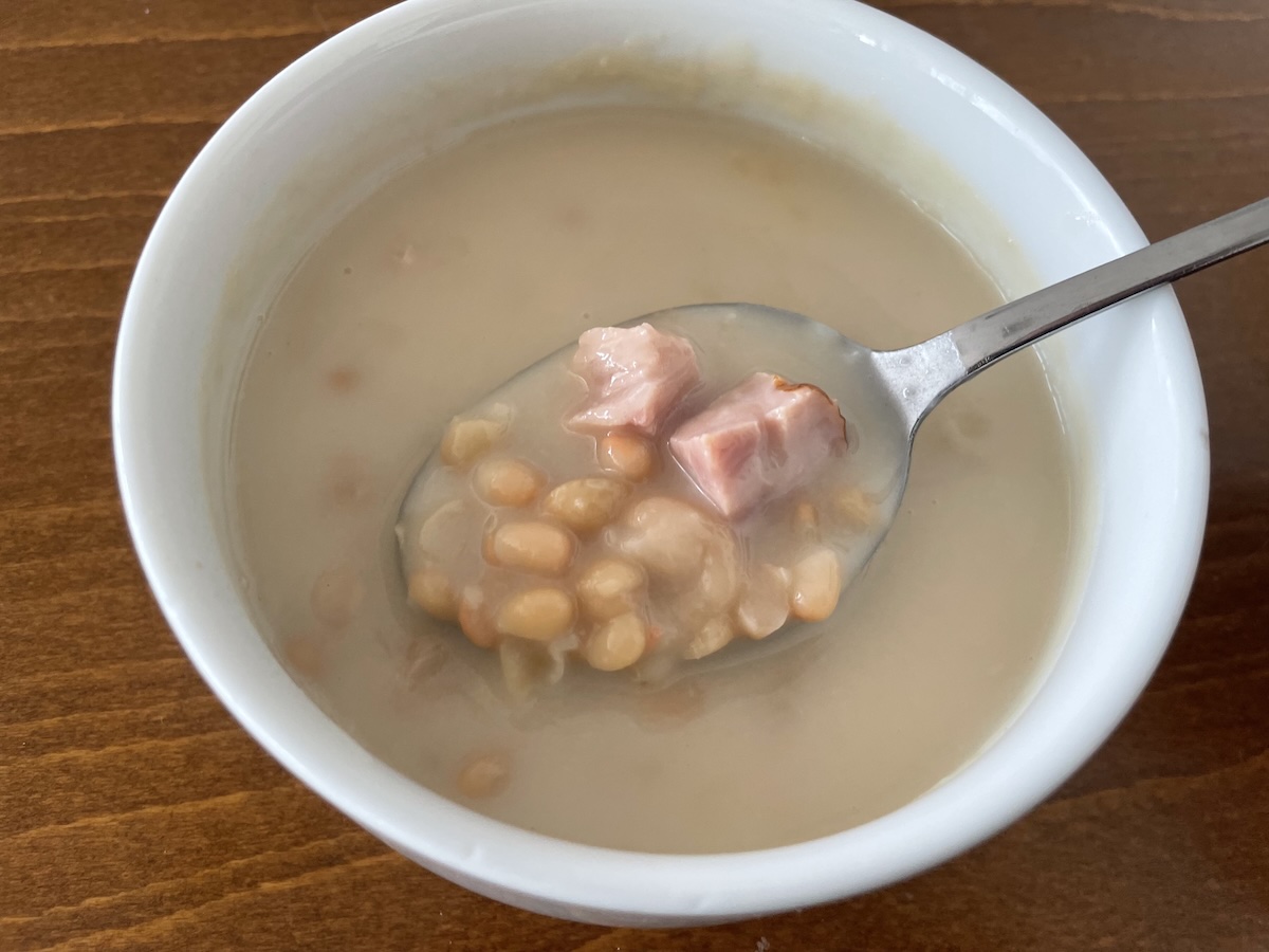 Uvarená biela fazuľa s kúskami údeného mäsa v bielej miske s lyžicou