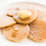 Americké palacinky pancakes posypané práškovým cukrom s maslom na bielom tanieri
