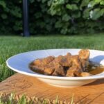 Bravčový guláš so zemiakmi v bielom hlbokom tanieri na drevenej doske v záhrade