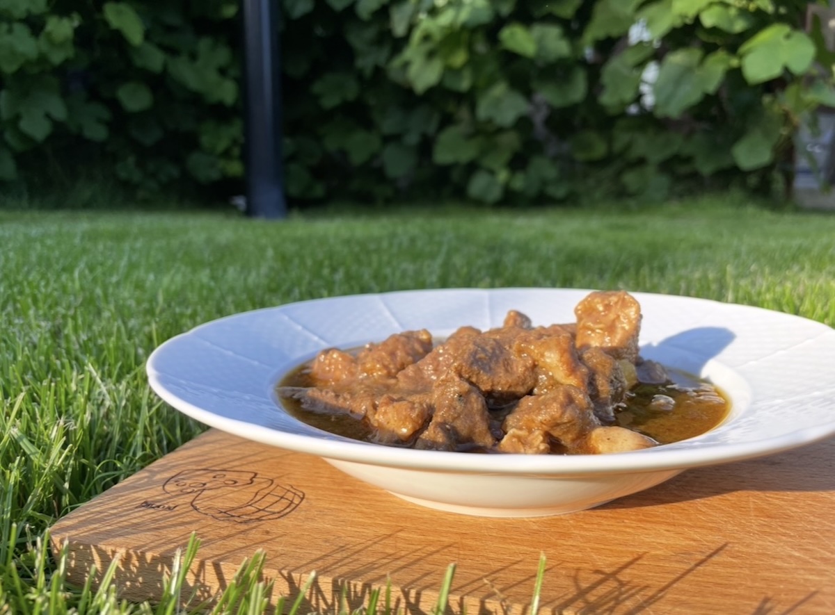 Bravčový guláš so zemiakmi v bielom hlbokom tanieri na drevenej doske v záhrade