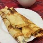 Prečo má cesto na palacinky hrudky – príčiny a riešenia Zlatisté zrolované palacinky so syrovou plnkou na bielom tanieri na červenom obruse