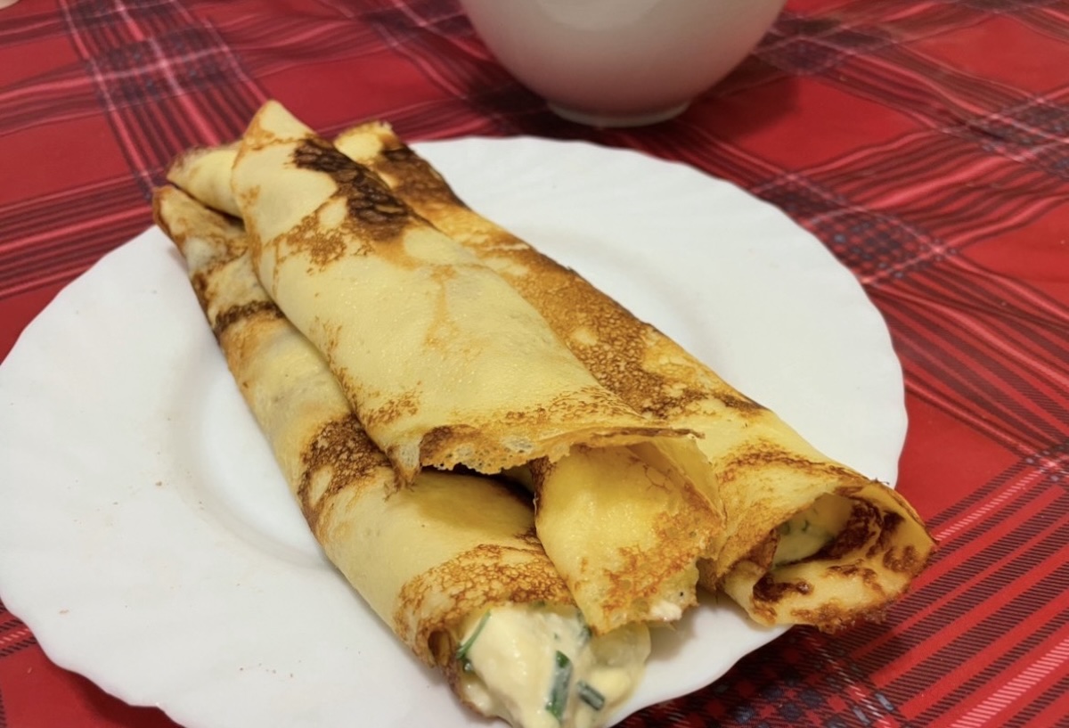 Zlatisté zrolované palacinky so syrovou plnkou na bielom tanieri na červenom obruse
