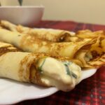Domáce palacinky plnené špenátom a syrom stočené na bielom tanieri