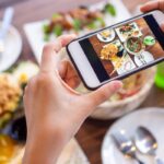 Človek fotí obed na mobile pri stole plnom jedla
