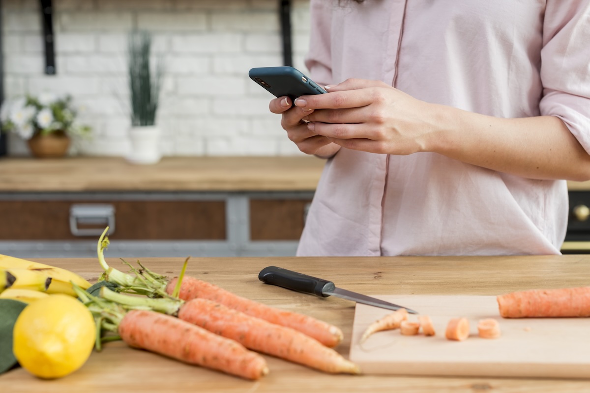 Žena hľadá recept na mobile pri krájaní mrkvy v kuchyni