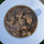 Kotlíkový guláš z hovädzieho mäsa v bielom hlbokom tanieri na tráve