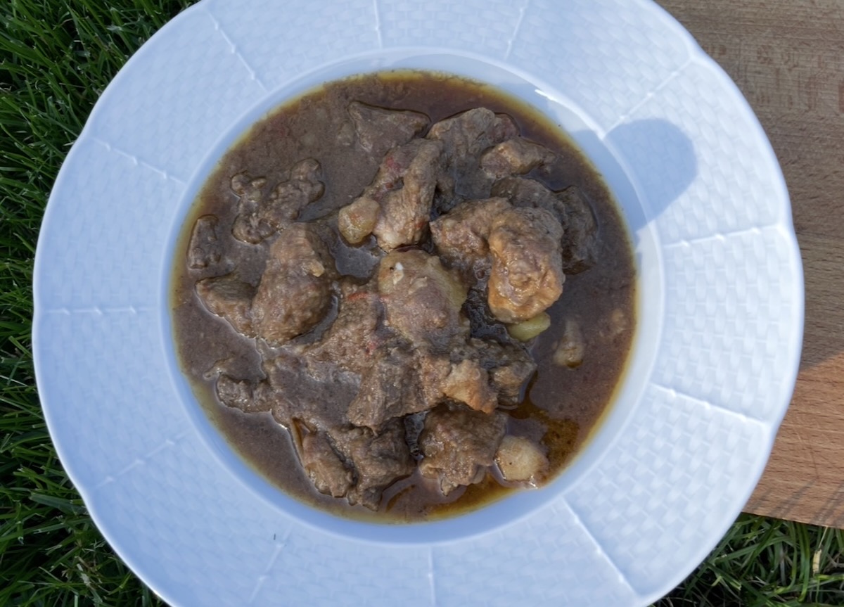 Kotlíkový guláš z hovädzieho mäsa v bielom hlbokom tanieri na tráve