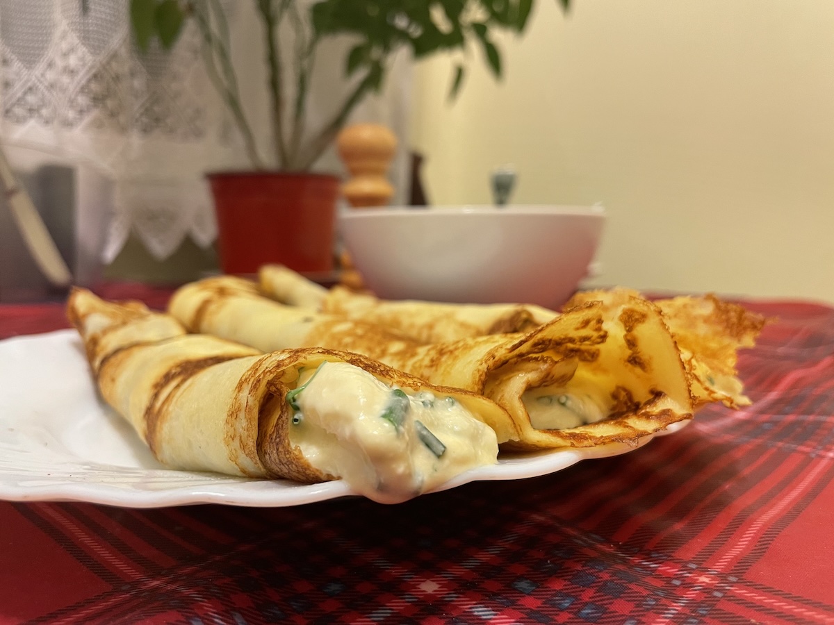 Zrolované tenké palacinky so syrovou plnkou na bielom tanieri na červenom obruse