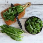 Čerstvé listy medvedieho cesnaku nakrájané na doske vedľa misy s nožom