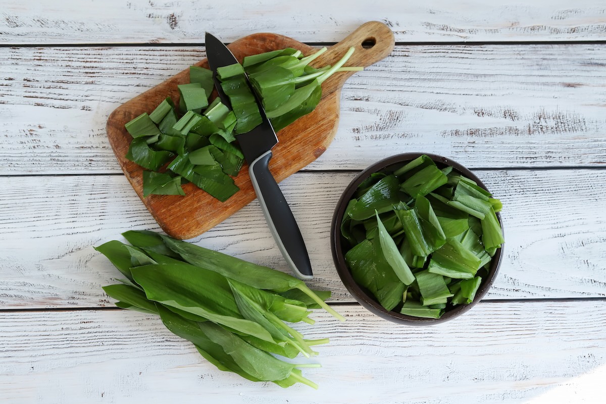 Čerstvé listy medvedieho cesnaku nakrájané na doske vedľa misy s nožom