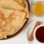 Tenké zlatisté palacinky na hlinenom tanieri s medom a čajom so škoricou