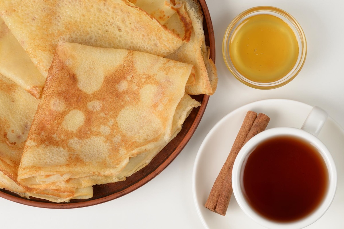 Tenké zlatisté palacinky na hlinenom tanieri s medom a čajom so škoricou