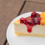 Naozaj pravý americký new york cheesecake Kúsok pravého amerického New York cheesecaku s čerešňovou omáčkou na bielom tanieri