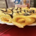 Zrolované tenké palacinky s čokoládou na bielom tanieri na červenom obruse