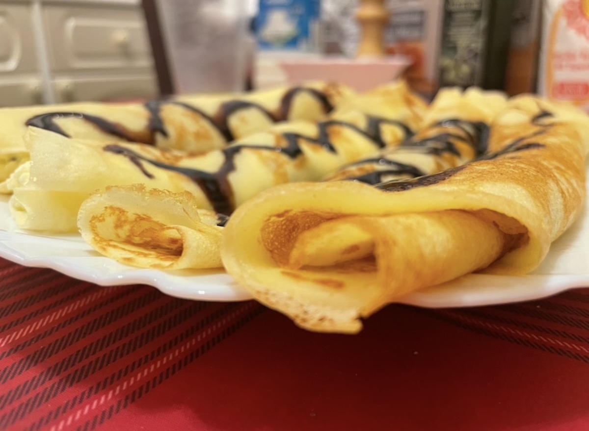 Zrolované tenké palacinky s čokoládou na bielom tanieri na červenom obruse