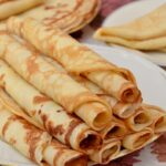 Tenké zlatisté palacinky zrolované do rúrky naukladané na bielom tanieri so zlatým okrajom