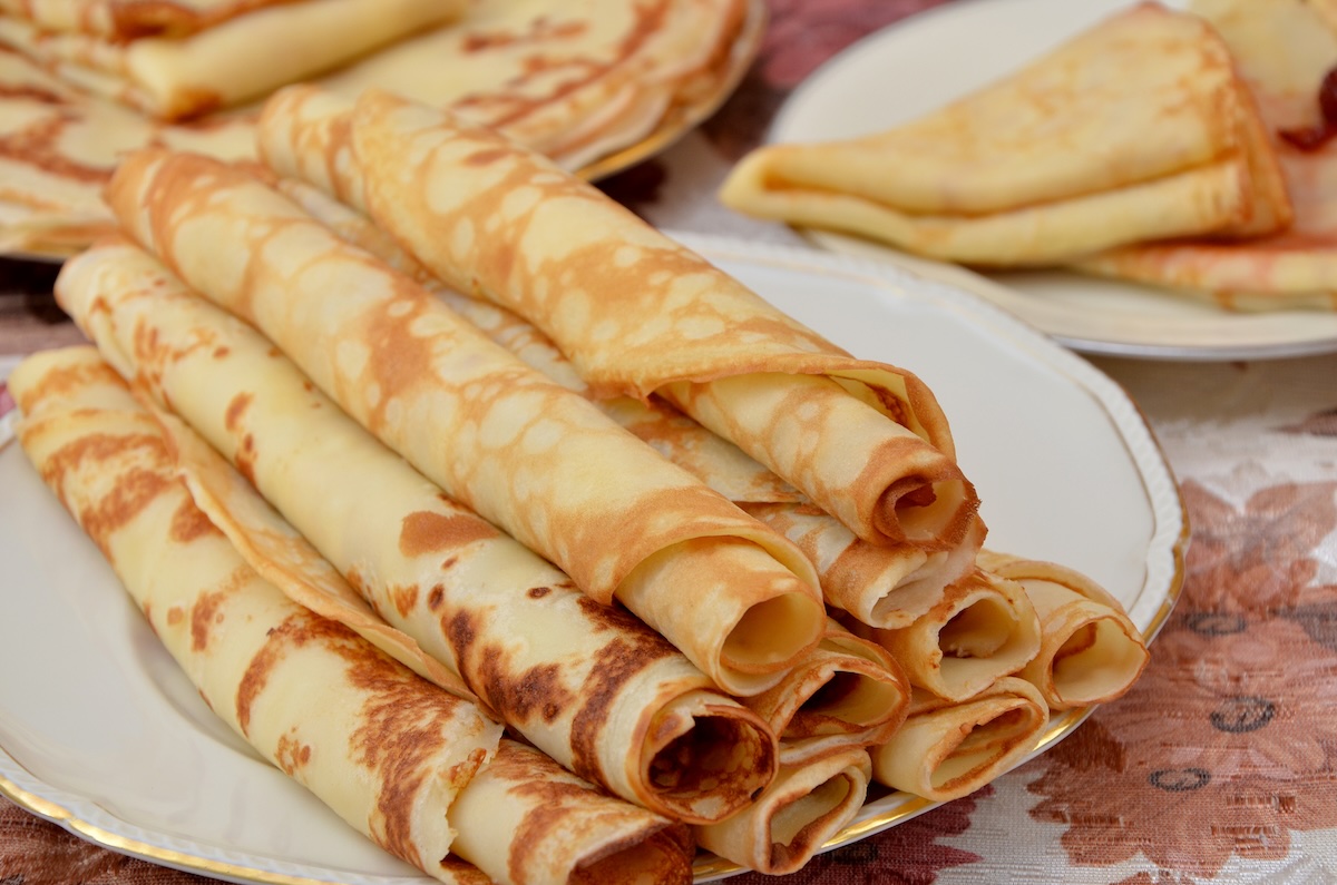 Tenké zlatisté palacinky zrolované do rúrky naukladané na bielom tanieri so zlatým okrajom