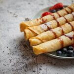 Tenké palacinky stočené do roliek posypané práškovým cukrom s čerstvým ovocím