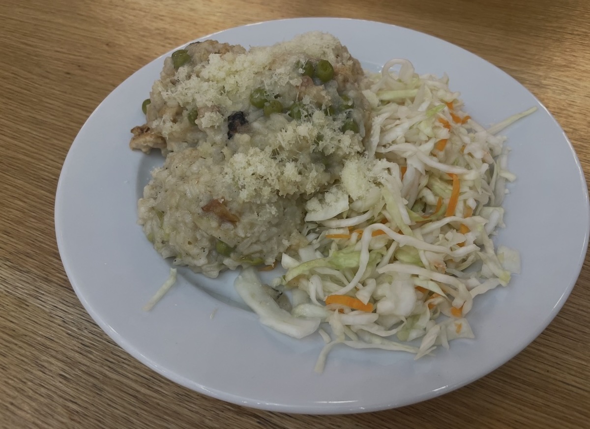 Krémové rizoto s kuracím mäsom a hráškom posypané parmezánom na bielom tanieri