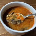 Šampiňónová polievka so zeleninou v bielom hrnčeku s lyžicou