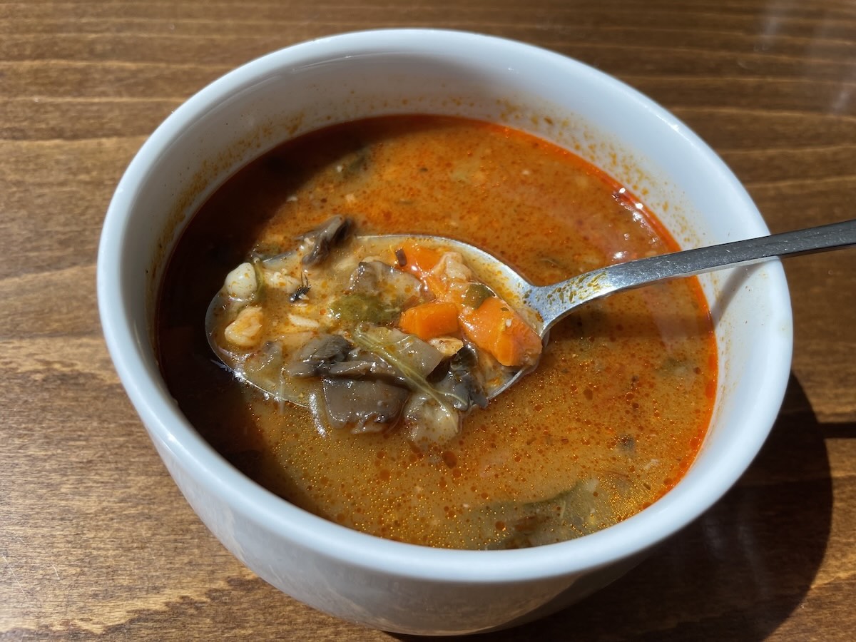 Šampiňónová polievka so zeleninou v bielom hrnčeku s lyžicou