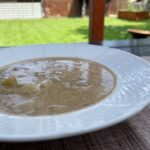 Šošovicová polievka na kyslo so zemiakmi v bielom hlbokom tanieri na terase so záhradou v pozadí