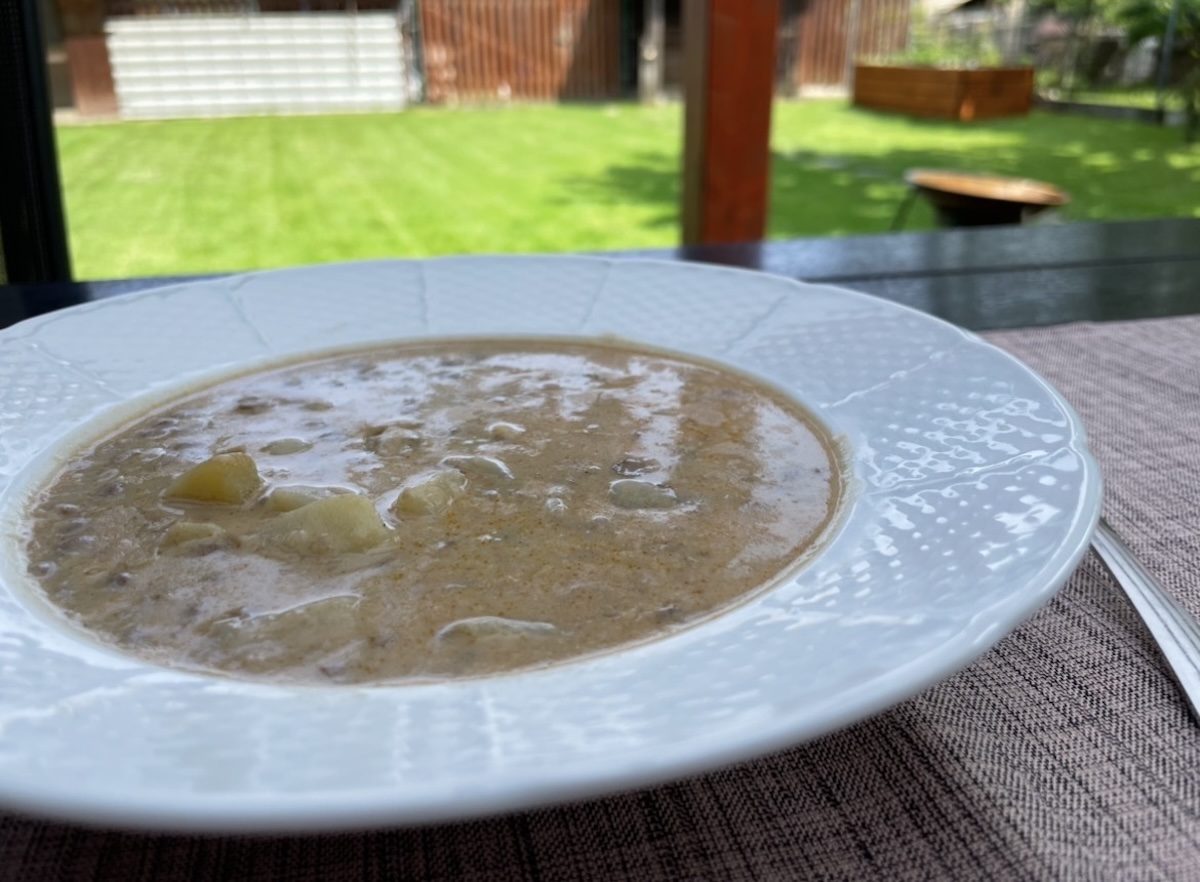 Šošovicová polievka na kyslo so zemiakmi v bielom hlbokom tanieri na terase so záhradou v pozadí