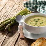 Krémová špargľová polievka v bielej miske s čerstvou špargľou