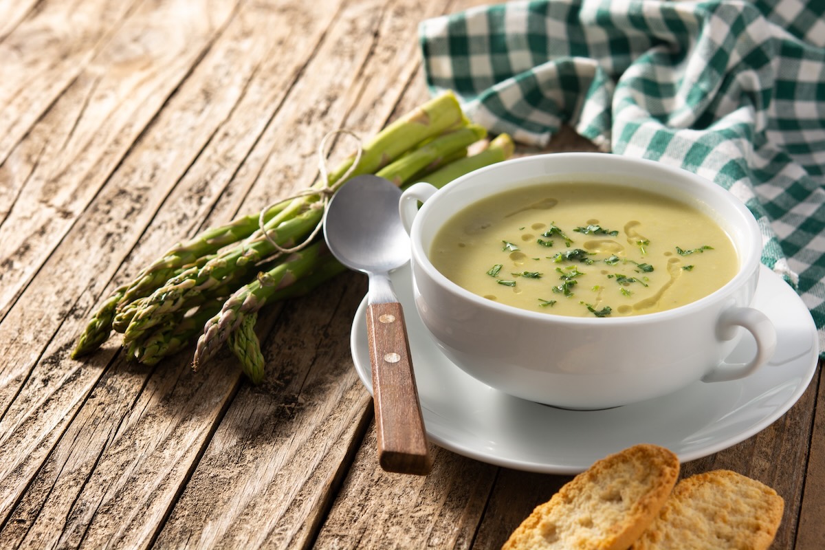 Krémová špargľová polievka v bielej miske s čerstvou špargľou