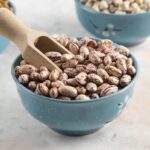 Suché strukoviny v modrých miskách — fazuľa, šošovica a hrach s drevenou naberačkou