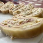 Syrová roláda nakrájaná na plátky s šunkovou a smotanovou náplňou na bielom tanieri