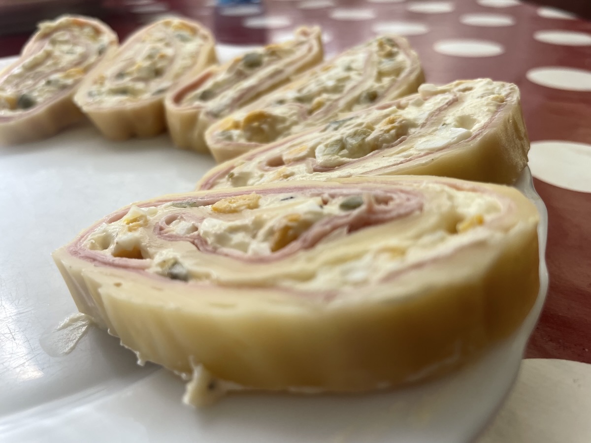 Syrová roláda nakrájaná na plátky s šunkovou a smotanovou náplňou na bielom tanieri