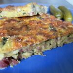 Veľkonočná baba nakrájaná na plátky s kyslými uhorkami na modrom tanieri