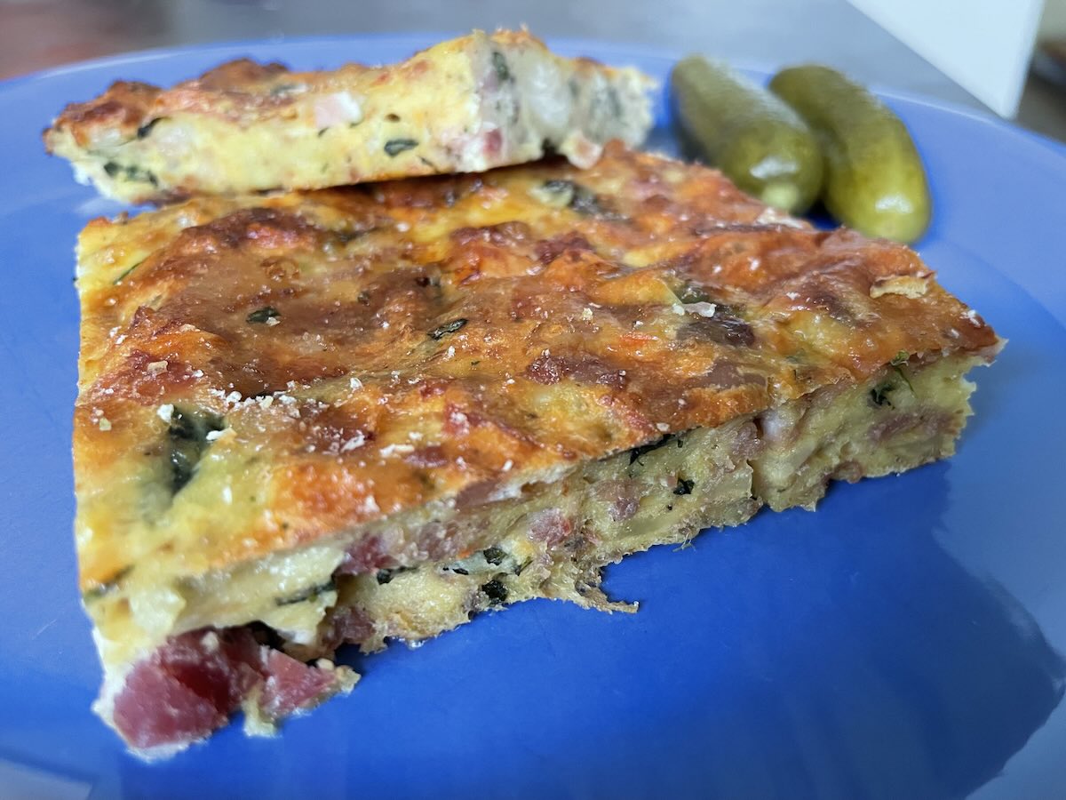 Veľkonočná baba nakrájaná na plátky s kyslými uhorkami na modrom tanieri