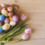 Veľkonočný košík s farebnými kraslicami a ružovými tulipánmi na drevenom stole