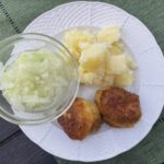 Vyprážaný karfiol s varenými zemiakmi a uhorkový šalátom na bielom tanieri