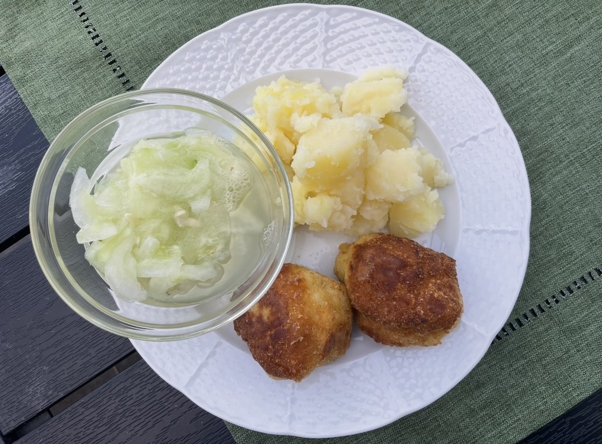 Vyprážaný karfiol s varenými zemiakmi a uhorkový šalátom na bielom tanieri