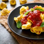 Jednoduchá omáčka na tortellini: paradajková s cesnakom a bazalkou Tortellini s paradajkovou omáčkou a čerstvou bazalkou na čiernom tanieri